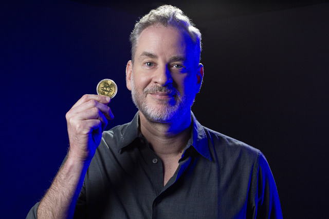Dan Stulbach segura uma moeda fictícia de Bitcoin; o ator faz staking