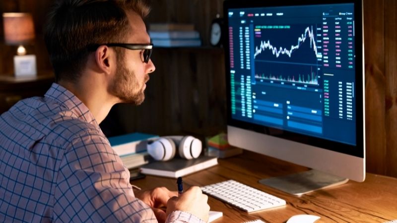 investidor sentado diante de tela de computador avaliando ações - mercado