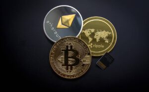 Imagem representando Criptomoedas, mostrando uma moeda de Bitcoin, de Ethereum e de Ripple. Falência dos bancos SVB