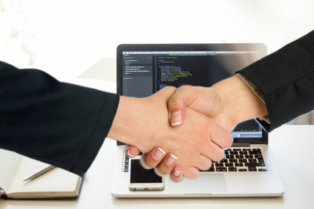 Imagem representando o tag along, mostrando duas pessoas apertando as mãos fazendo um acordo em frente a um computador. mercado