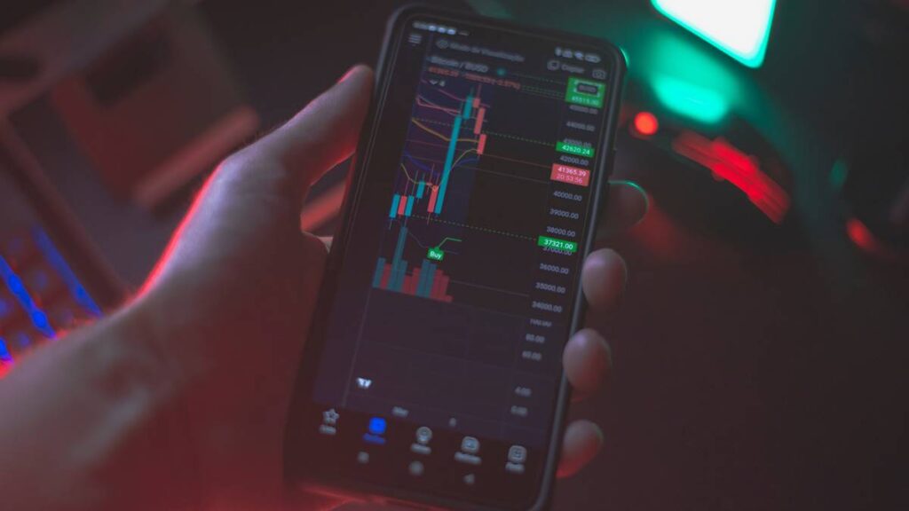 Imagem representando o mercado de capitais, mostrando uma tela de celular com gráficos e indicadores financeiros.