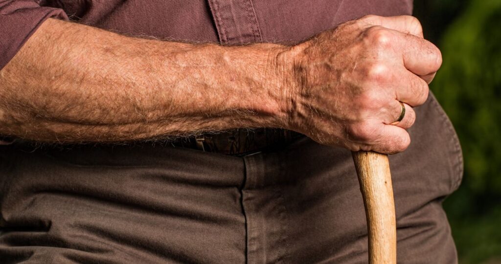 Braço de um homem idoso segura um cajado de madeira