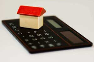 Imagem representando a hipoteca, mostrando uma miniatura de imóvel junto a uma calculadora.