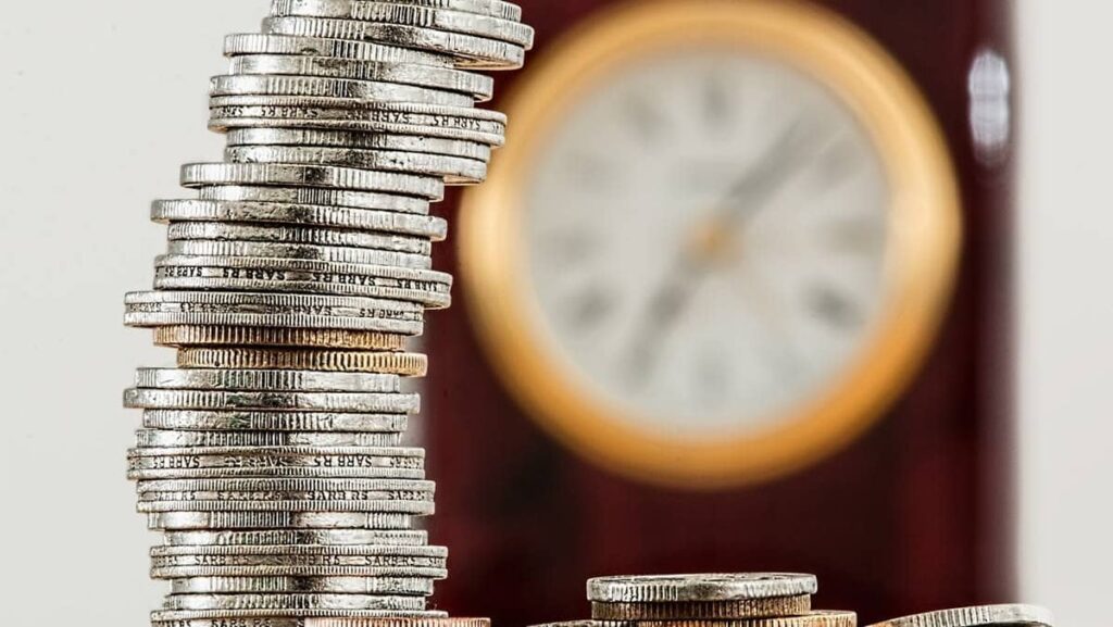Imagem representando os juros futuros, mostrando uma pilha de dinheiro com um relógio ao fundo.