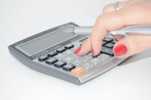 Imagem representando o DIRF, a Declaração do Imposto sobre a Renda Retido na Fonte, contendo uma pessoa usando uma calculadora.