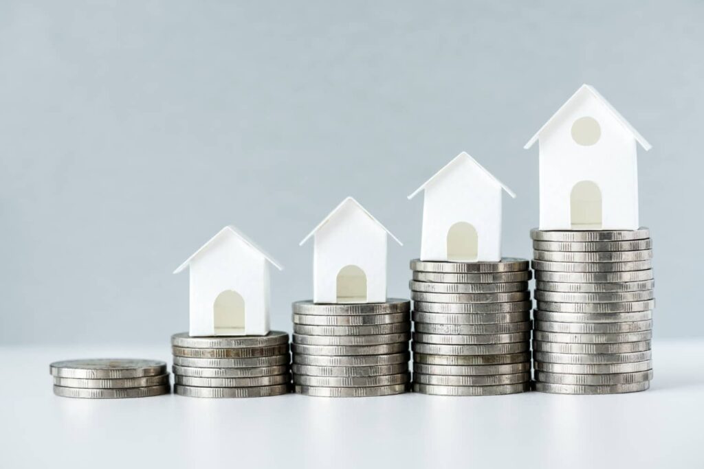 Imagem com moedas e casas ao fundo para representar a tributação dos FIIs. fundos imobiliários imóveis