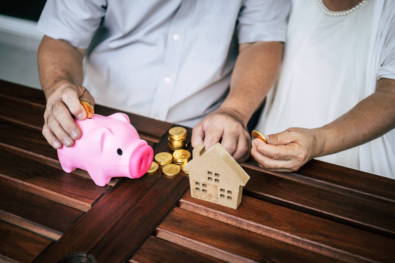Imagem de duas pessoas com moedas, casa de brinquedo e um cofre de porquinho para representar tributação de previdência privada.