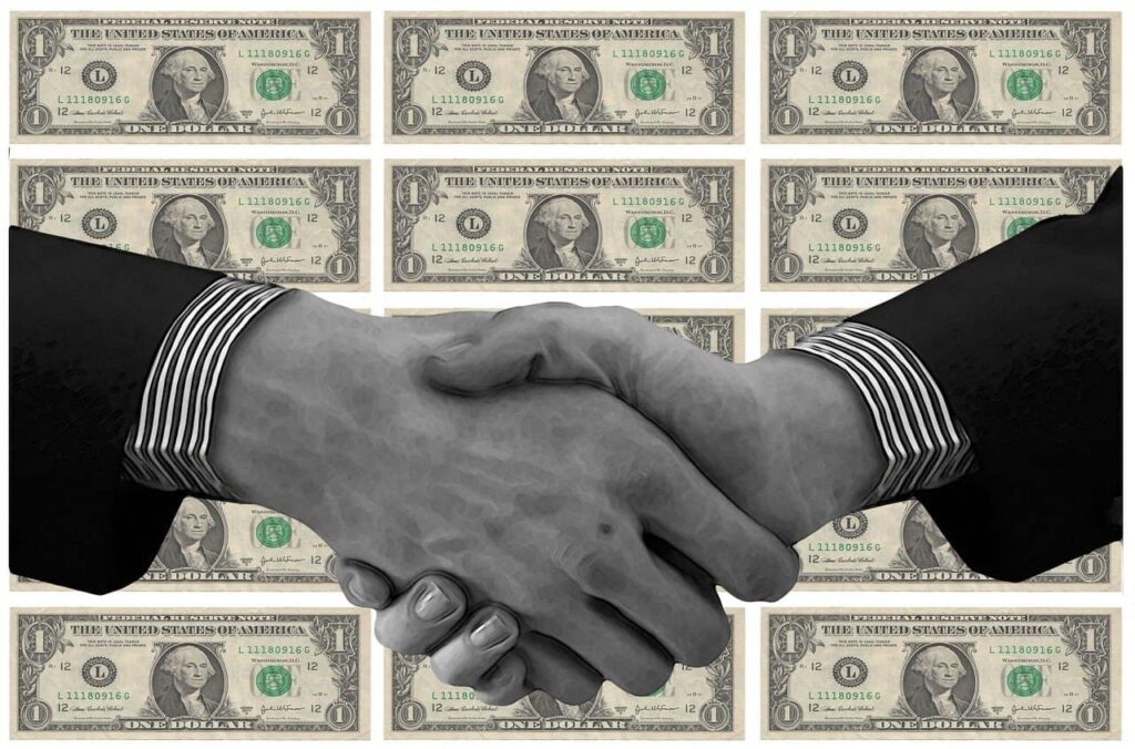 Imagem de um aperto de mãos com dólares ao fundo para representar o investimento em Letra de Câmbio (LC). dólar dividendos árabes vale3 vale